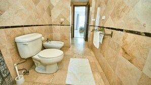 A bathroom with two toilets, a bidet, a towel rack, and a marble floor.