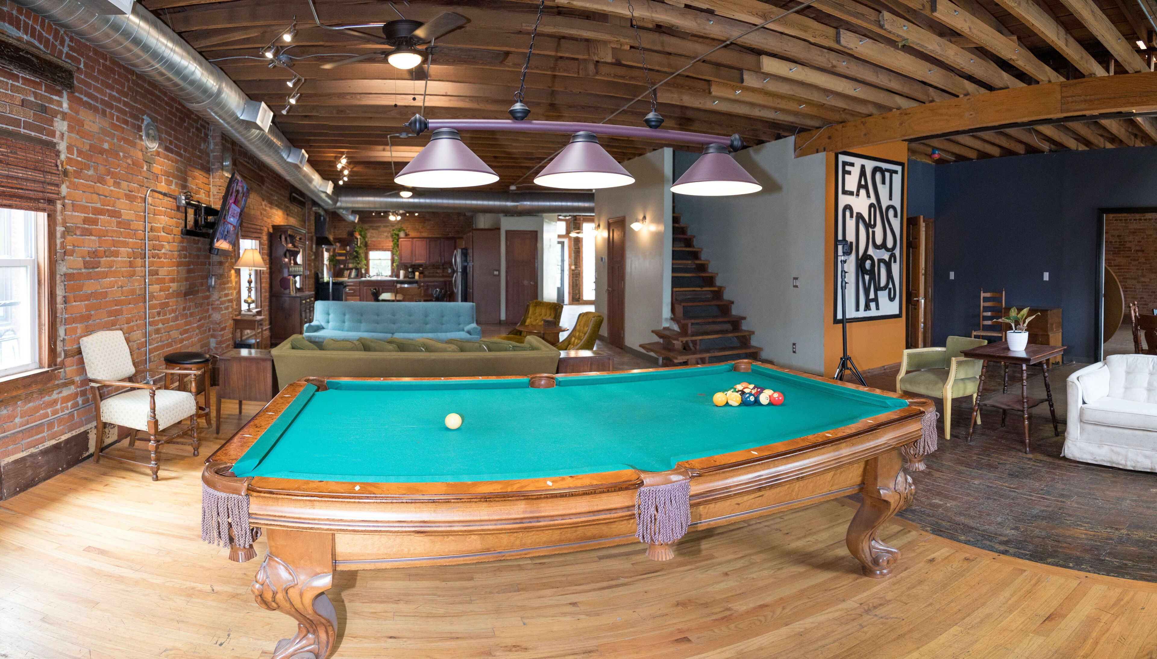 A spacious room with a pool table, wooden flooring, and a brick wall.