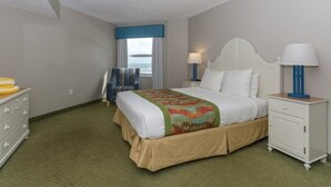 A hotel room with a bed, bedside tables, a dresser, a window with curtains, and a view of the ocean.