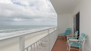 A balcony with a view of the ocean, featuring two blue and white lounge chairs.