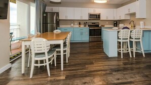 A compact kitchen with white cabinets, a wooden dining table, and bar stools.
