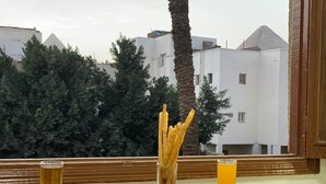 A table with food and drinks, a view of buildings, and a palm tree. - Sphinx Safari (Giza)
