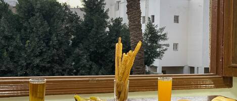 A table with food and drinks, a view of buildings, and a palm tree.