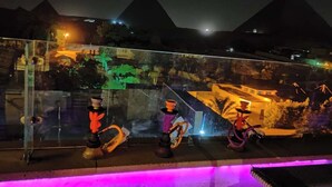 A glass railing with hookahs and a view of pyramids at night. - Sphinx Safari (Giza)