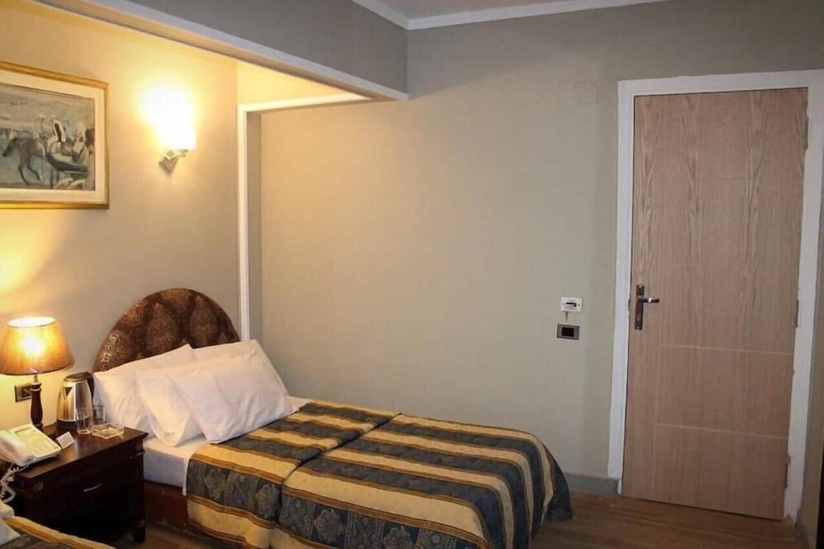 A hotel room with a bed, bedside lamp, a painting on the wall, and a wooden door.