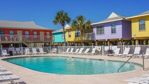 A pool area with a clear blue pool, surrounded by colorful buildings and white sun loungers.