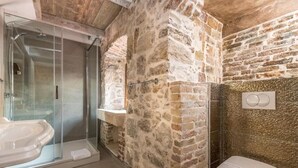 Une salle de bain avec une douche à parois de verre, des toilettes blanches et des murs en pierre.