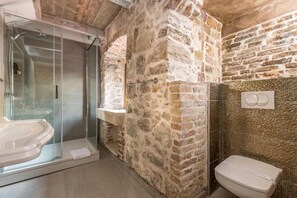 A bathroom with a glass shower enclosure, a white toilet, and stone walls. - Historic Plaza Varos Split (Split)