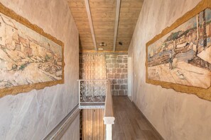 A hallway with stone walls and wooden ceiling beams, featuring two large paintings on either side.
