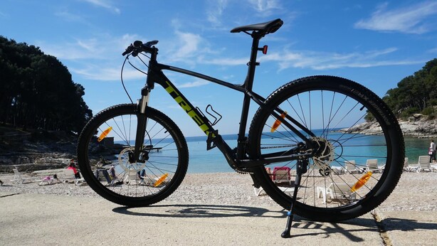 Un vélo tout-terrain est garé sur une surface en béton, près d’une plage, sous un ciel dégagé.