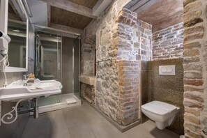 Un baño con pared de piedra, un lavabo blanco y un inodoro.
