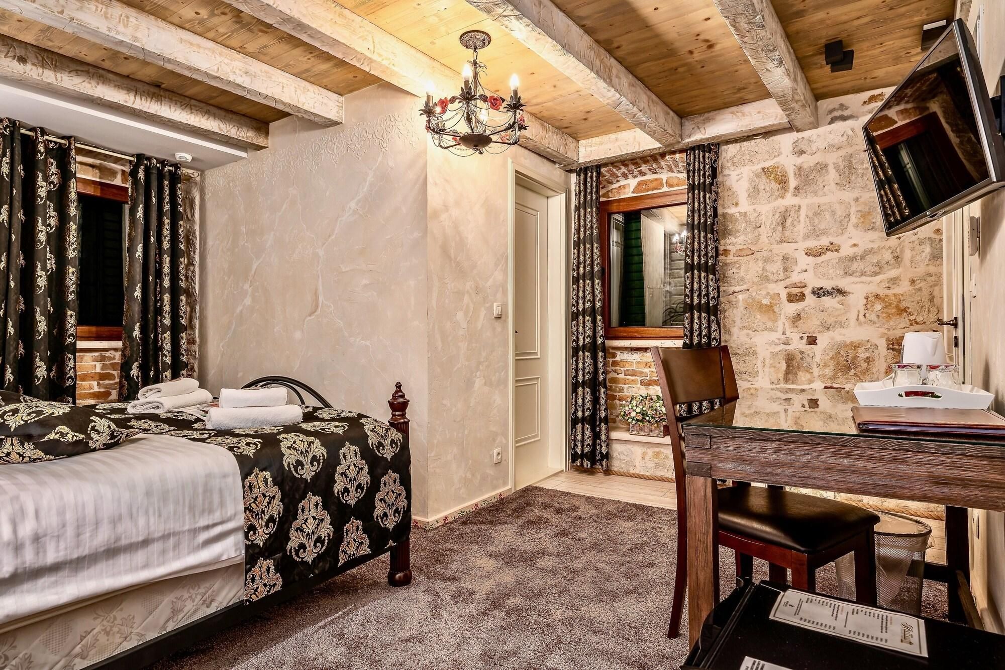 A bedroom with a bed, a desk, a chair, a chandelier, and a stone wall.