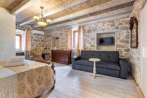 Una habitación con cama, sofá, una mesita, televisión y pared de piedra.