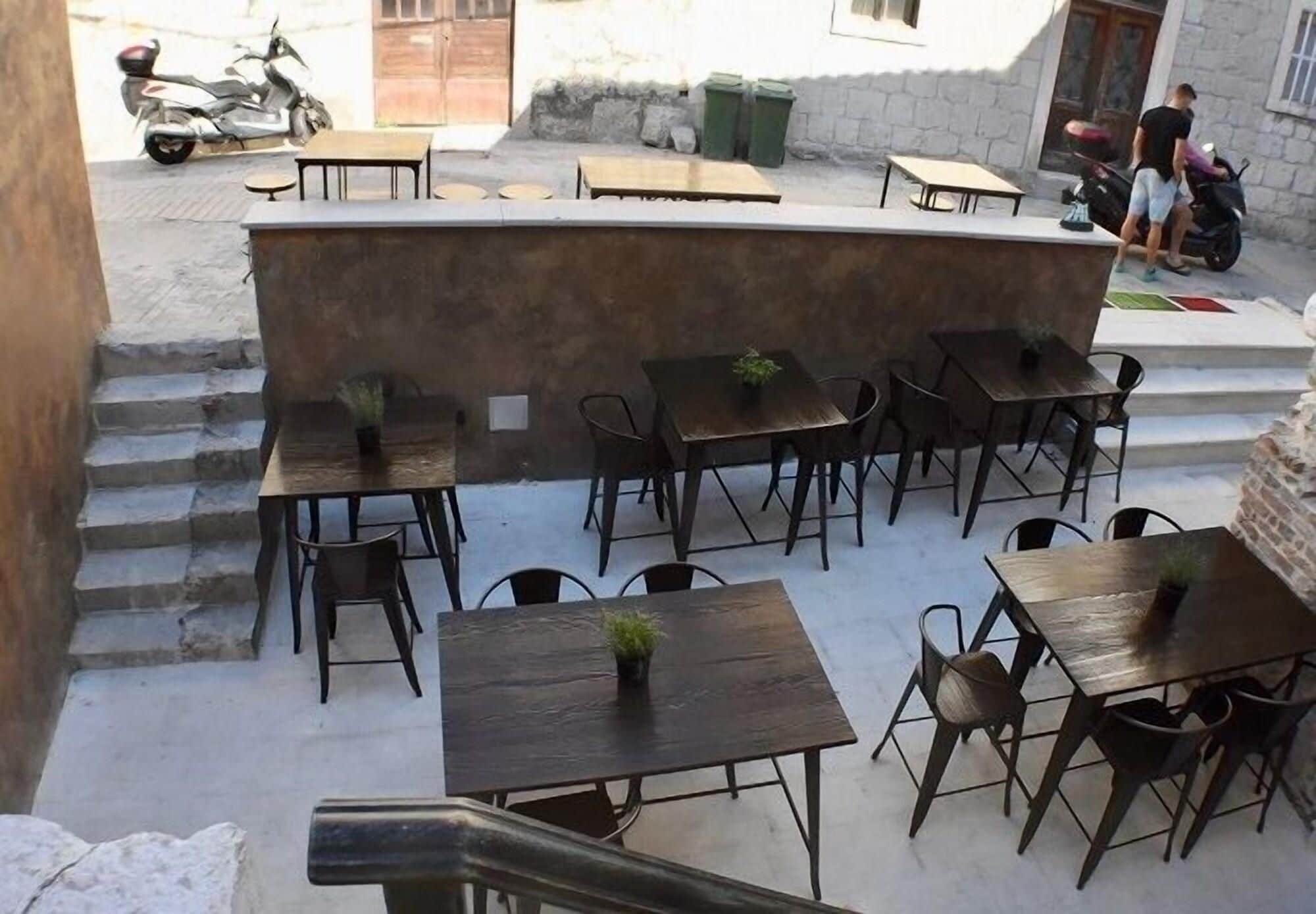An outdoor seating area with multiple tables and chairs, a small counter, and a few scooters parked nearby.