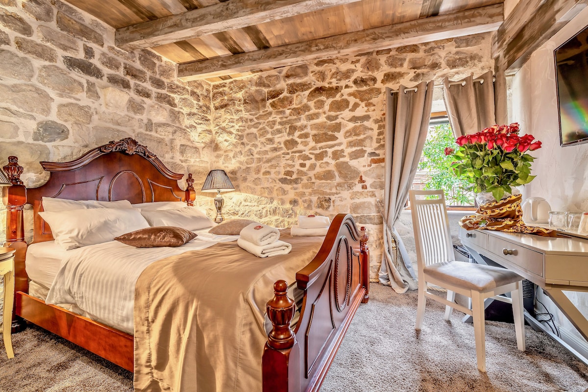 A stone-walled bedroom with a wooden bed, a desk, and a chair.