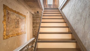 Eine Treppe mit Holzdielen und Metallgeländern, die zu einem Raum mit Steinwand und einem gerahmten Bild führt.