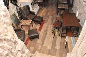 Una habitación con pared de piedra, suelo de madera, sofá de cuero marrón, una pequeña mesa y una zona de bar con taburetes.