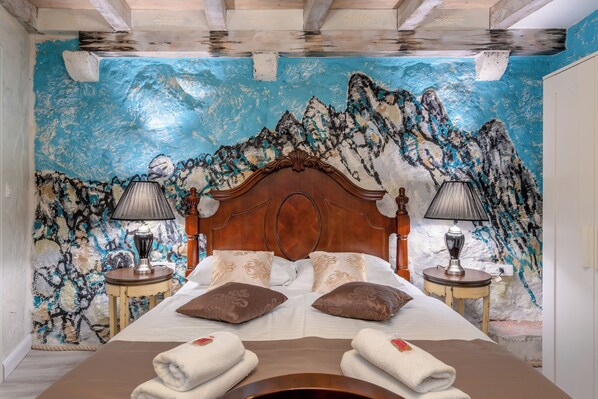 Un dormitorio con una cama grande, dos mesitas de noche con lámparas y un mural de montañas en la pared.