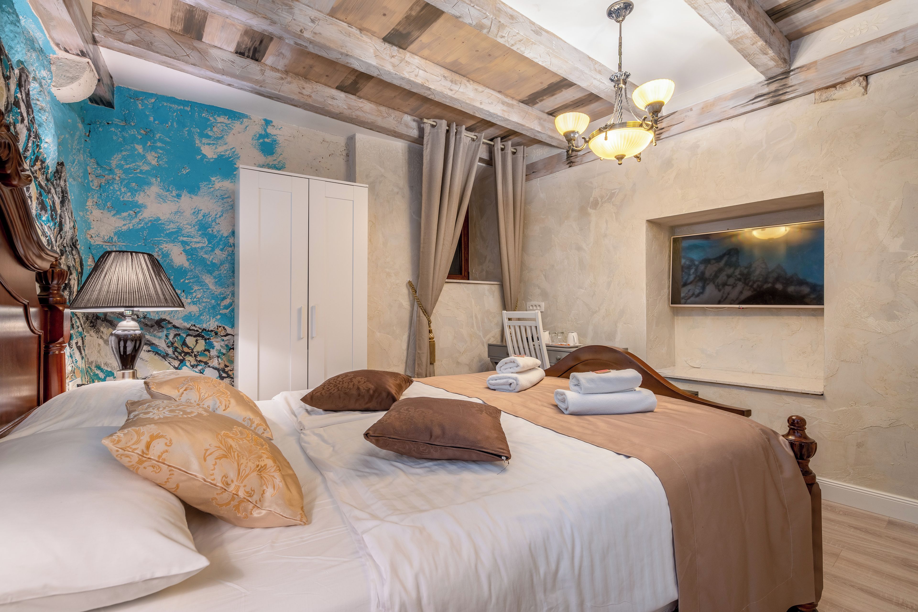 Een hotelkamer met een bed, nachtkastje, lamp, schilderij en een houten plafond.