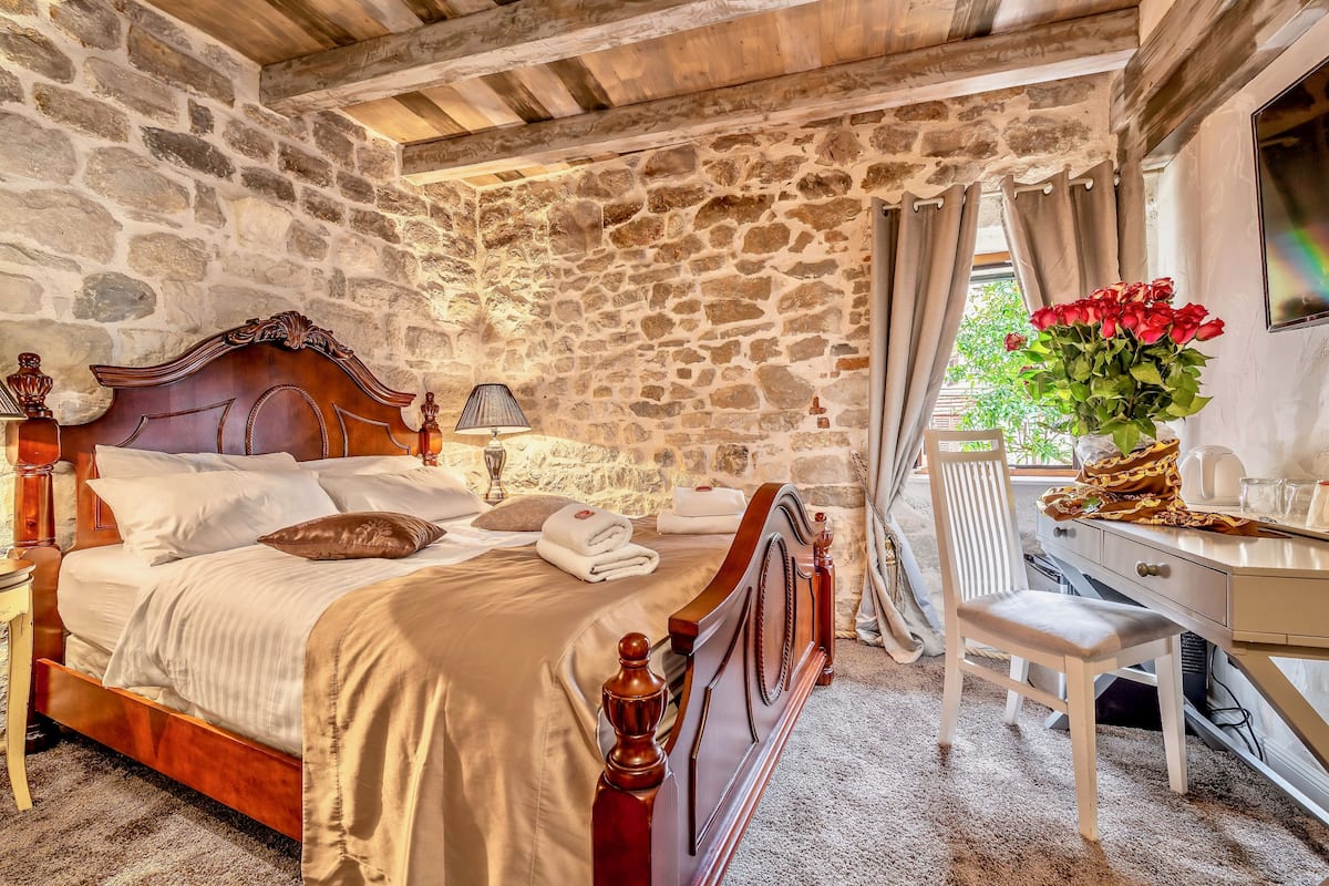 Un dormitorio con paredes de piedra, una cama de madera, un escritorio y una silla.
