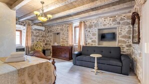Ein Zimmer mit einem Bett, einer Couch, einem kleinen Tisch, einem Fernseher und einer Steinswand.