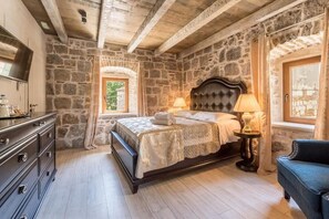 A bedroom with stone walls, a bed with a headboard, a dresser, and a window with curtains. - Historic Plaza Varos Split (Split)