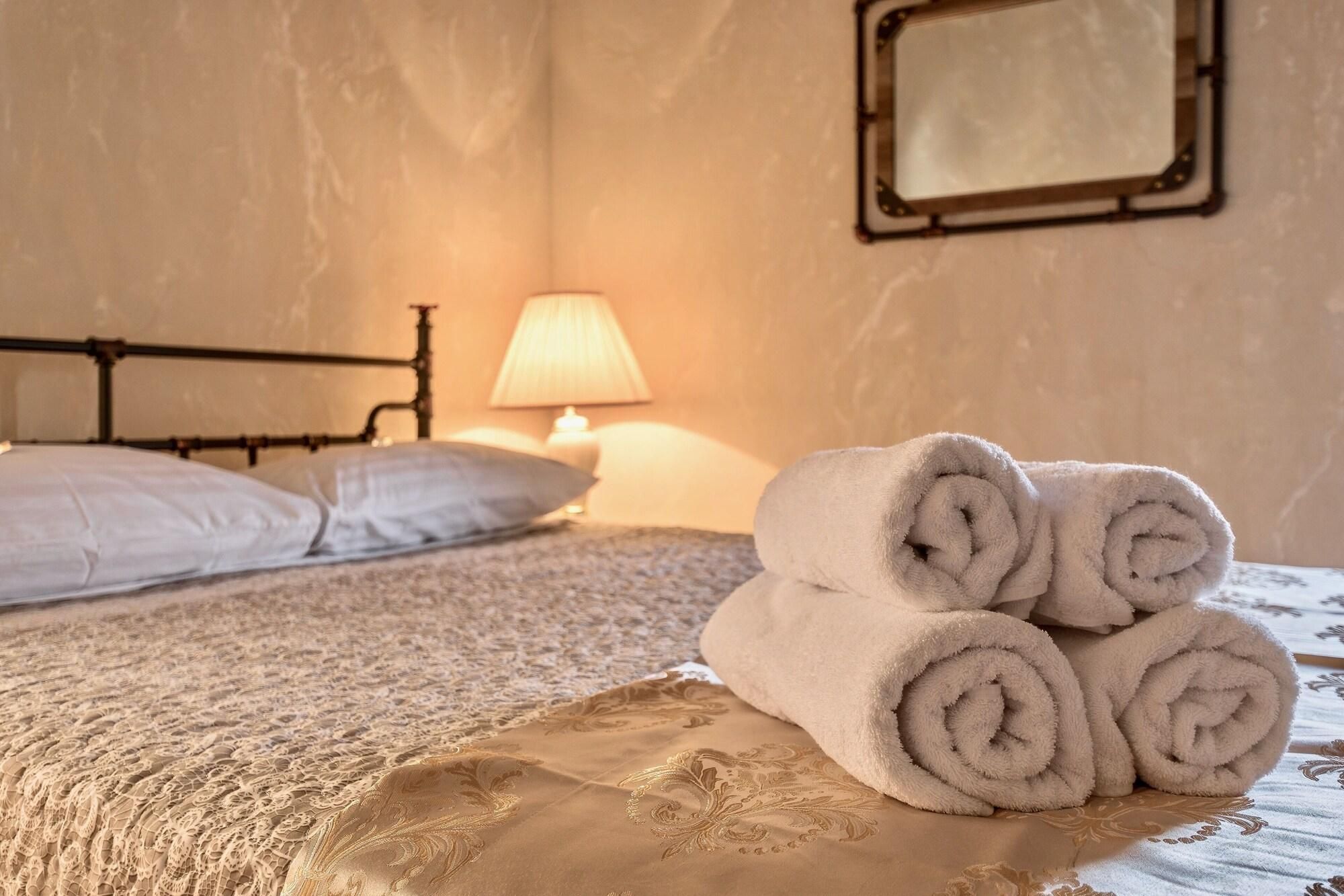 A neatly made bed with rolled towels, a lamp, and a mirror on the wall.