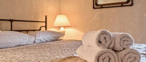 A neatly made bed with rolled towels, a lamp, and a mirror on the wall.