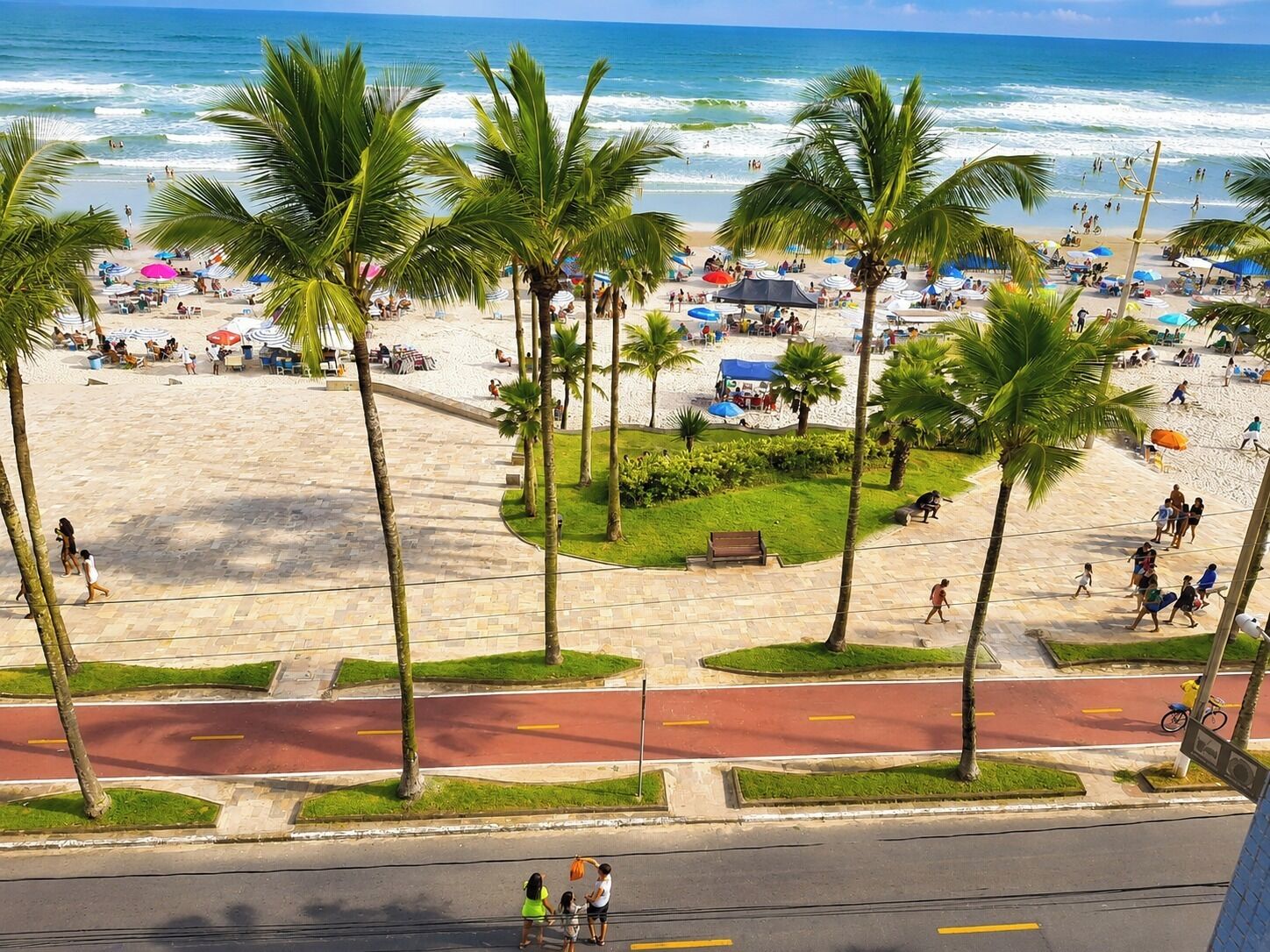 Ein Strand mit Palmen, einem Sandbereich und einer Straße mit Zebrastreifen.