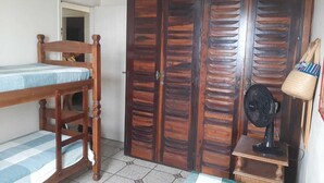 Une chambre avec un lit en bois, une armoire, un ventilateur et une petite table.