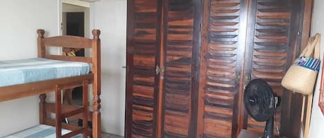 A bedroom with a wooden bed, a wardrobe, a fan, and a small table.