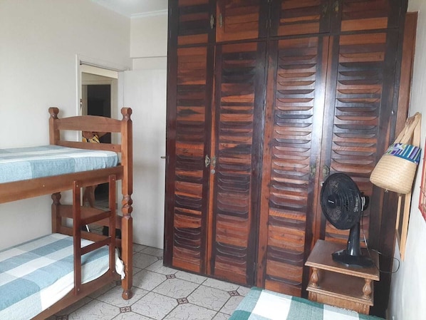 A bedroom with a wooden bed, a wardrobe, a fan, and a small table.