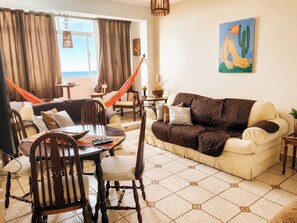 A living room with a sofa, chairs, a dining table, and a hammock. - Apartment overlooking the ocean. (SP)