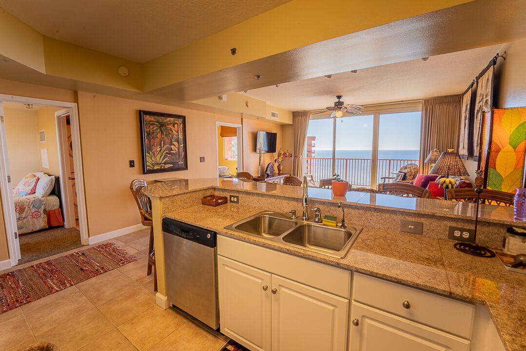 A kitchen with a dishwasher, double sink, and a view of the ocean.