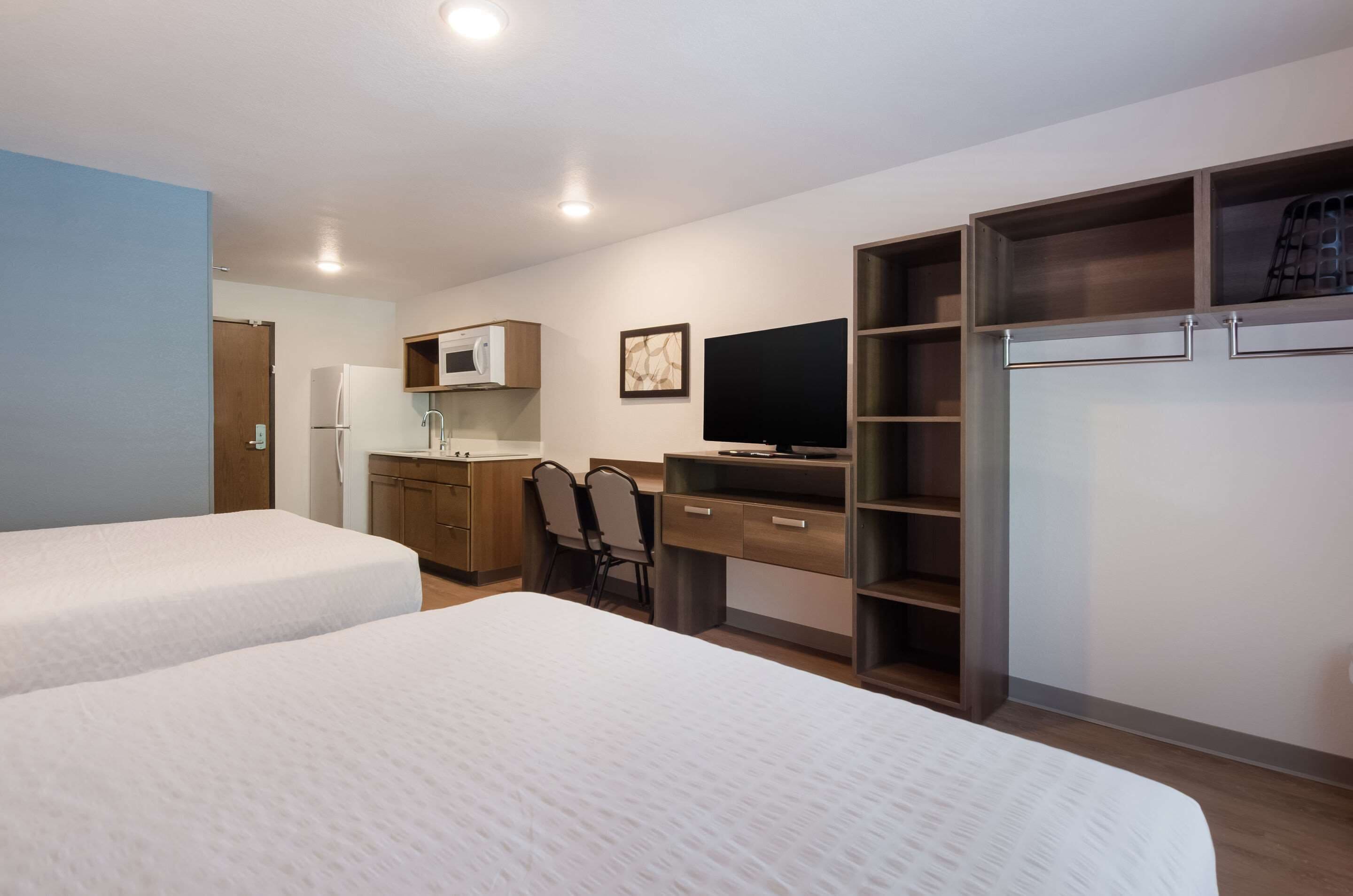 Een hotelkamer met twee bedden, een bureau met stoel, een televisie, een magnetron en een kledingkast.