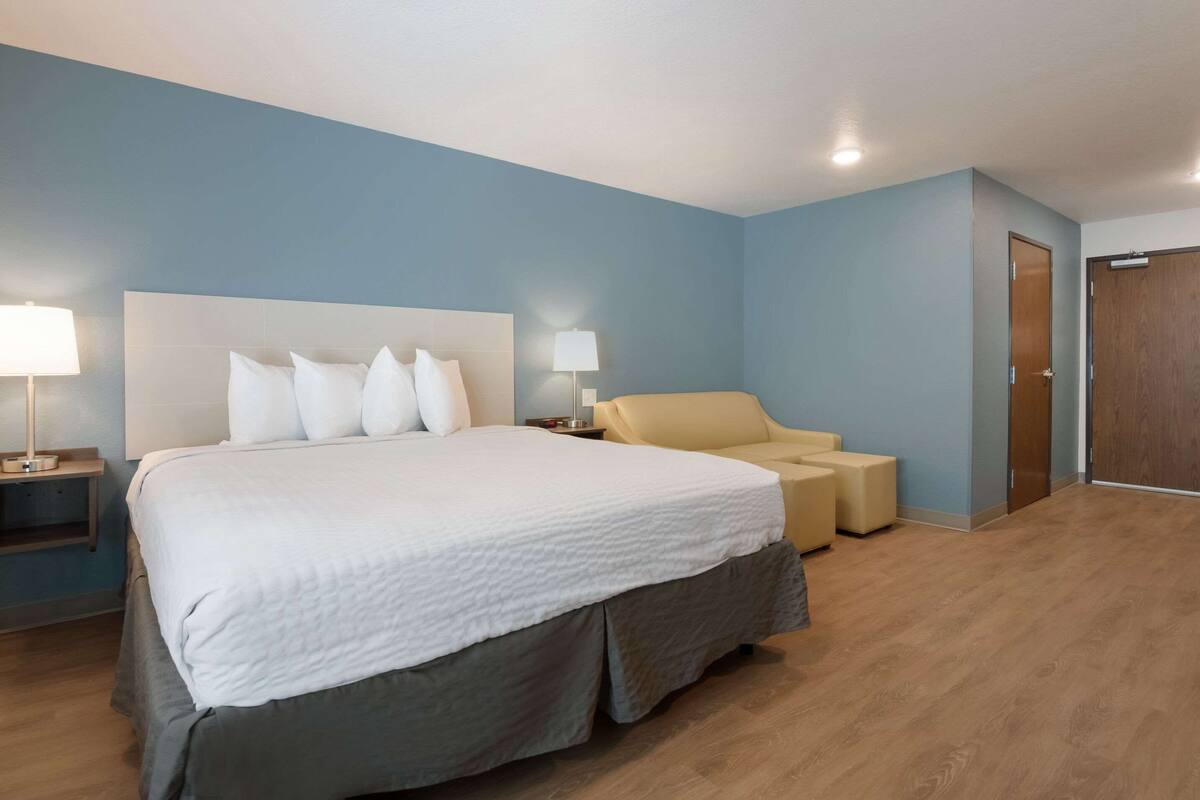 A hotel room with a large bed, two bedside lamps, a chair, a small table, and a door.