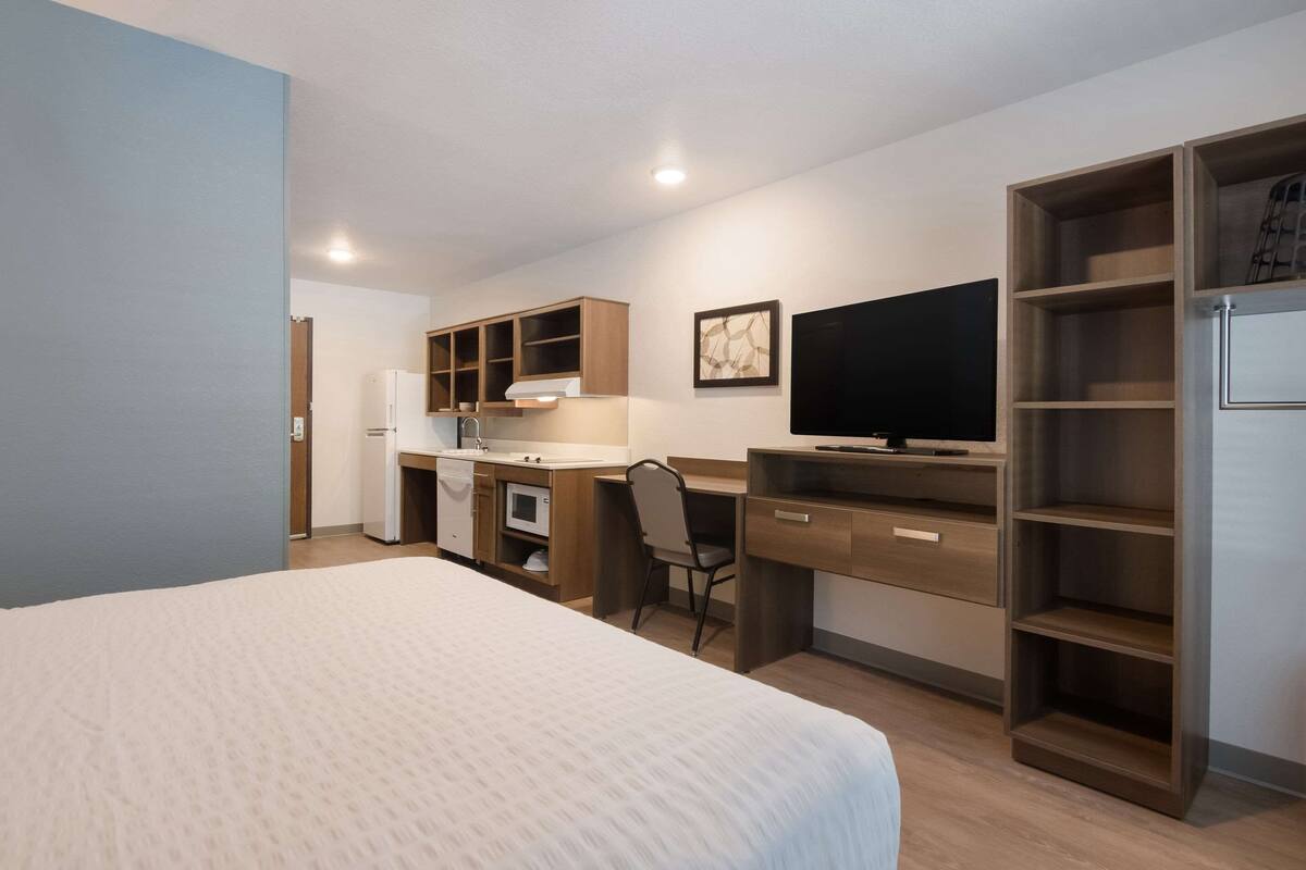 A hotel room with a bed, a desk with a chair, a television, and a wardrobe.