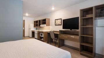 A hotel room with a bed, a desk with a chair, a television, and a wardrobe.