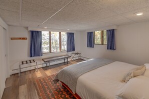 Une chambre à coucher avec un grand lit, un banc, une fenêtre avec des rideaux et un radiateur.