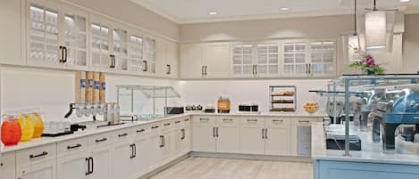 A spacious kitchen with white cabinets, a breakfast bar, and a coffee station.