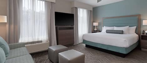 A hotel room with a bed, a TV, a ceiling fan, and a large window with curtains.