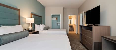 A hotel room with two beds, a TV, a dresser, and a lamp.