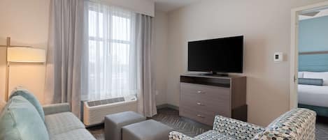 Ett hotellrum med en soffa, en pall, en tv och en säng med en blå sänggavel.