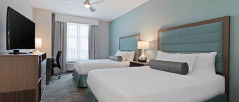 A hotel room with two beds, a desk, a television, and a ceiling fan.