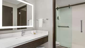 Un baño moderno con un espejo grande, un lavabo blanco, una cabina de ducha con mampara de cristal y un perchero para toallas.