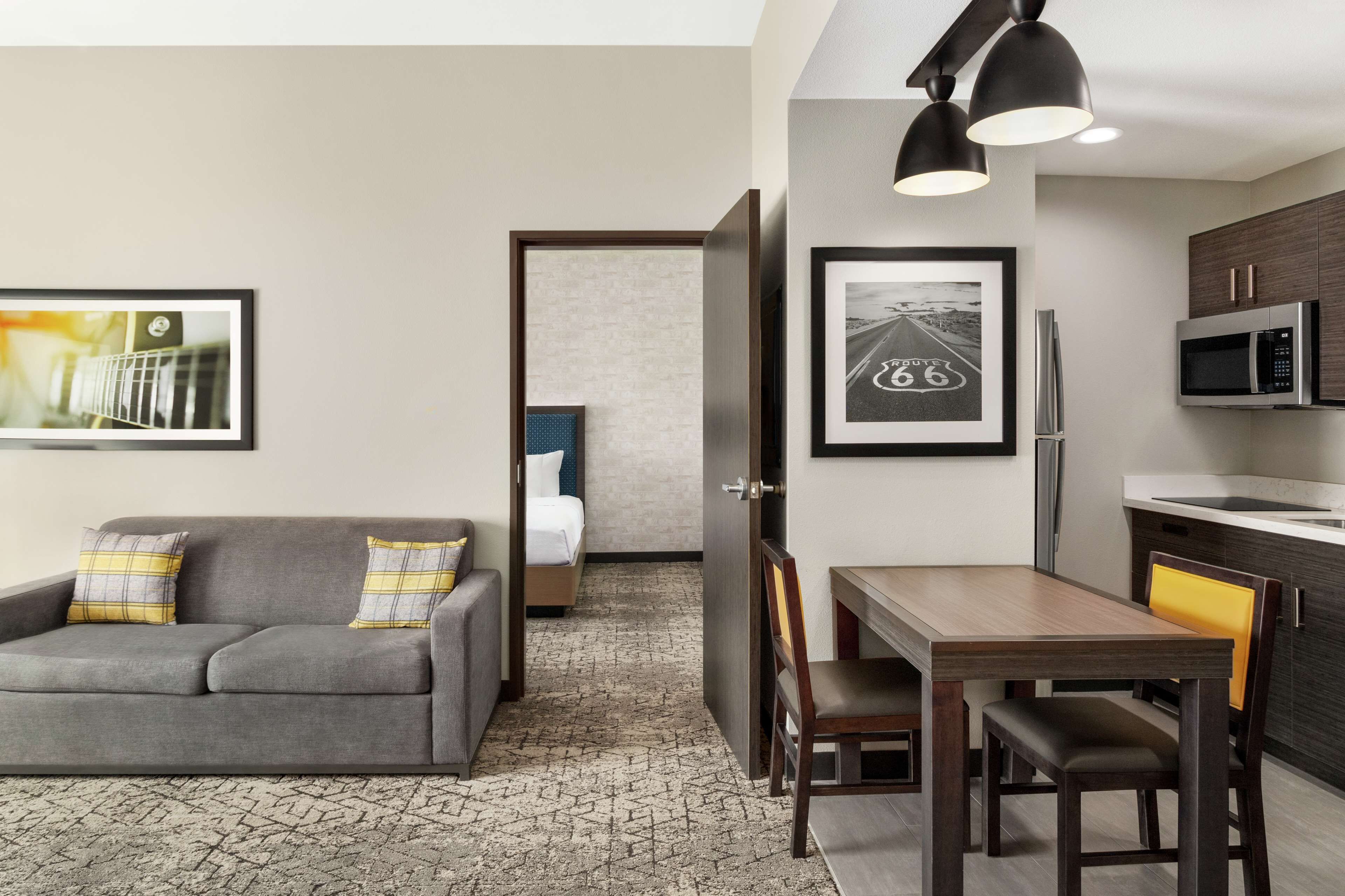 Une chambre d’hôtel de taille réduite, avec un canapé gris, une petite table à manger et un coin cuisine.