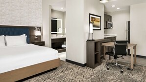 Quarto de hotel moderno com uma cama grande, uma mesa com cadeira, um espelho e um quadro na parede.