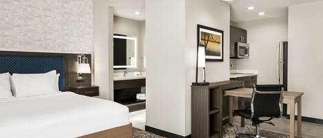 A modern hotel room with a large bed, a desk with a chair, a mirror, and a painting on the wall.