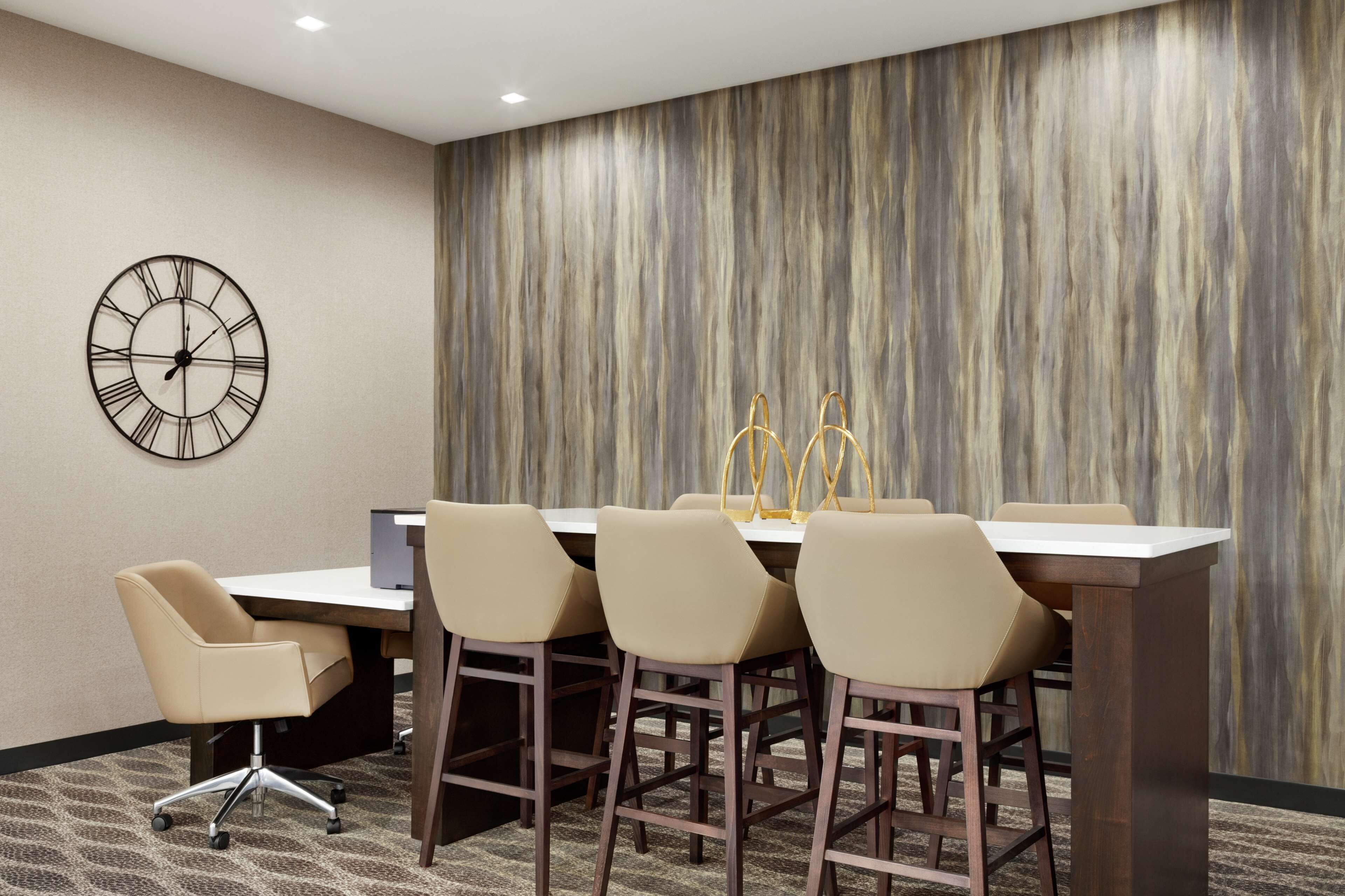 Un salón de conferencias con una mesa redonda, cuatro sillas, un reloj y un panel decorativo en la pared.