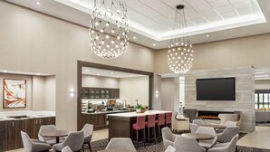 Um saguão moderno de hotel com bar, área de estar, cozinha e uma TV.